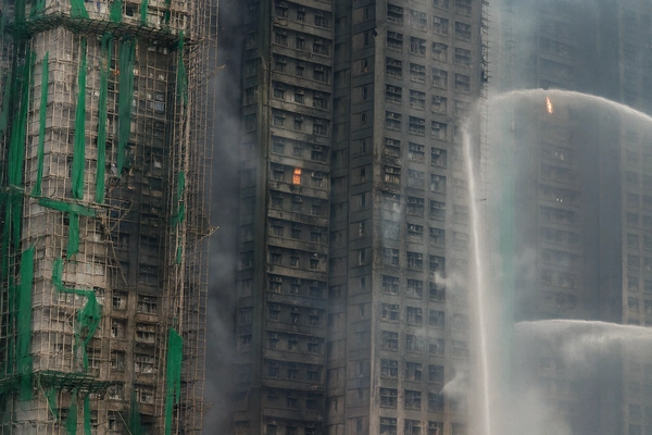 Hong Kong high-rise fire showing firefighters spraying water onto burning residential towers wrapped in bamboo scaffolding during a major blaze in Tai Po.